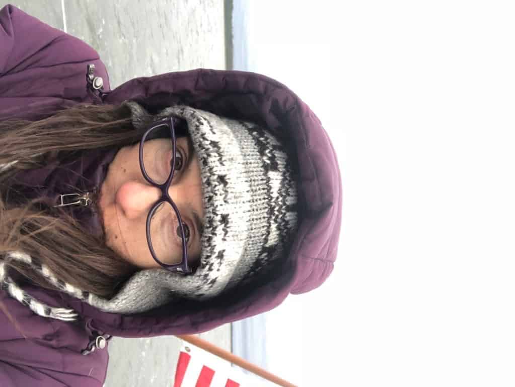 a woman on a sailboat, in a winter jacket, looking miserable. The photos is flipped sideways to demonstrate life at an angle.