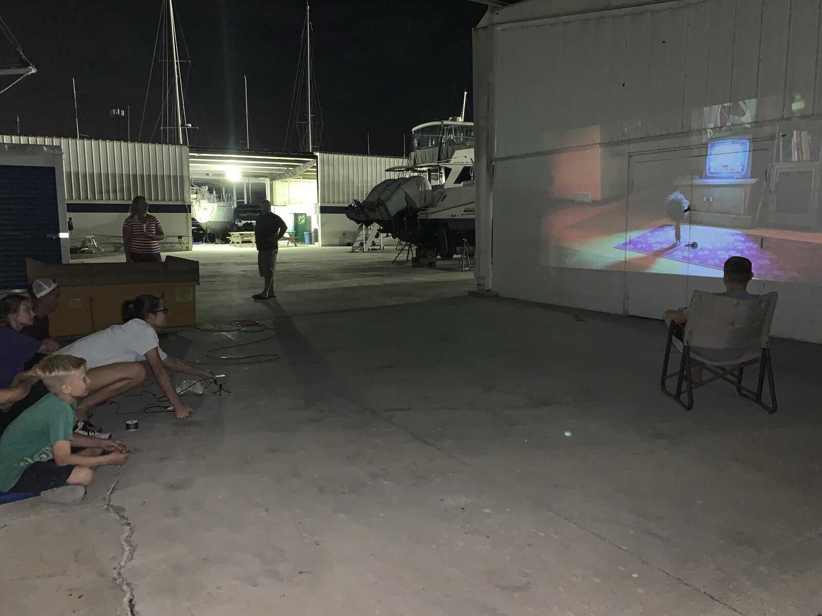 children watching a movie with a projector, on the wall of a boat yard utility building. 
