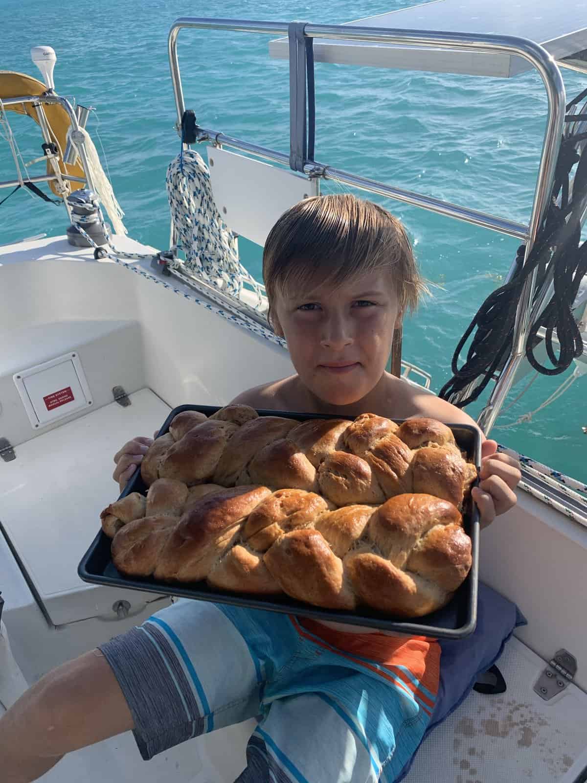 a boy holding a pan with home-baked braided bread, on a sailboat.