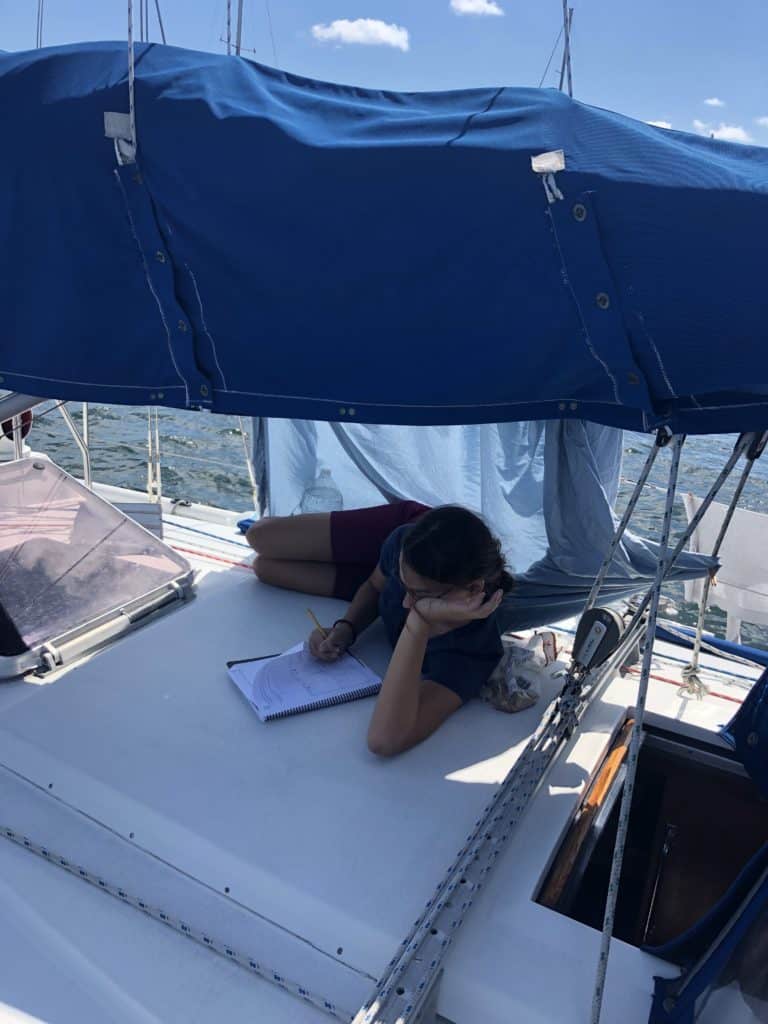 a girl on a boat, reading and a sheet behind her hung for shade
