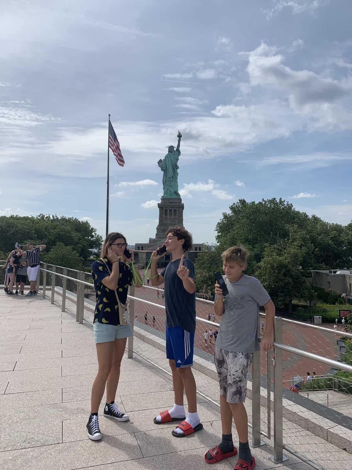 The kids by the statue of liberty with pretend cell phones