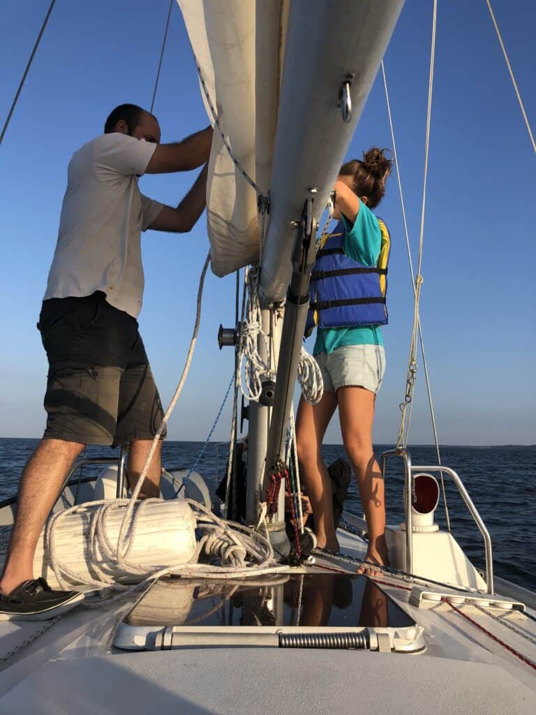 two people fixing the main sail. The man is wearing Sperry sailing shoes