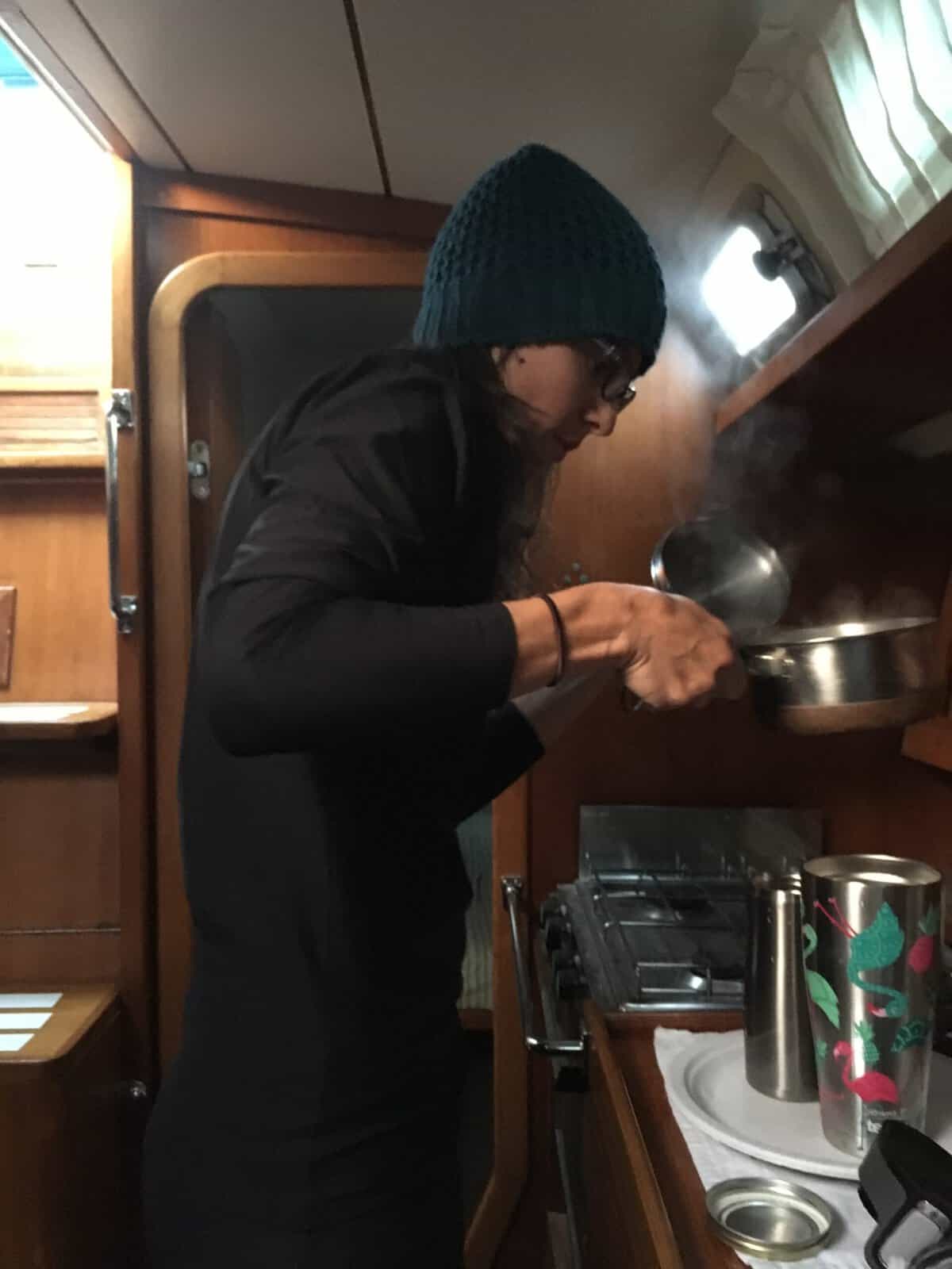 woman cooking in a hat, in the galley of a cold boat