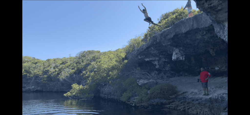 a boy jumping off a rock into a blue hole, in Bahamas