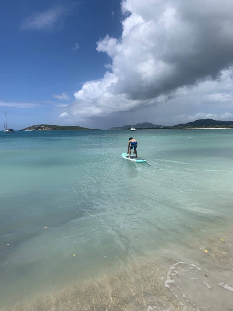 a boy on a paddle board at Sun Bay Beach with blue green water all around him