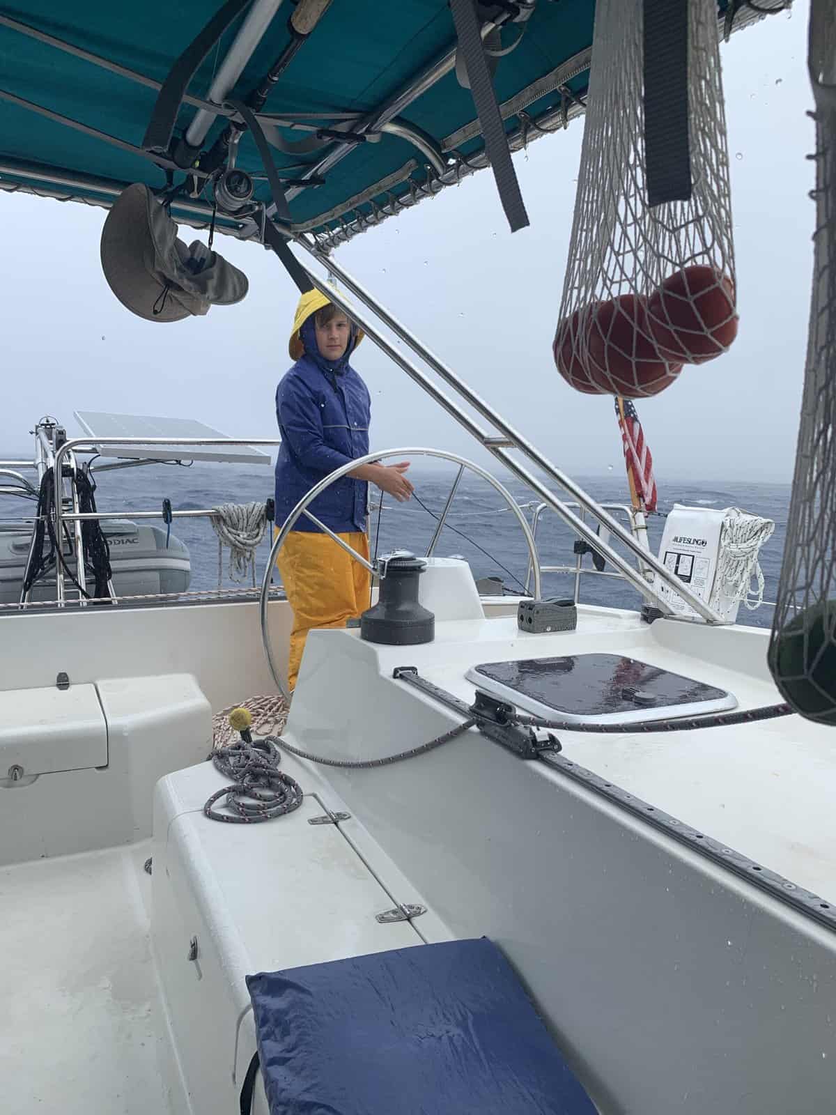 a boy wearing foul weather jacket and pants on a sailboat
