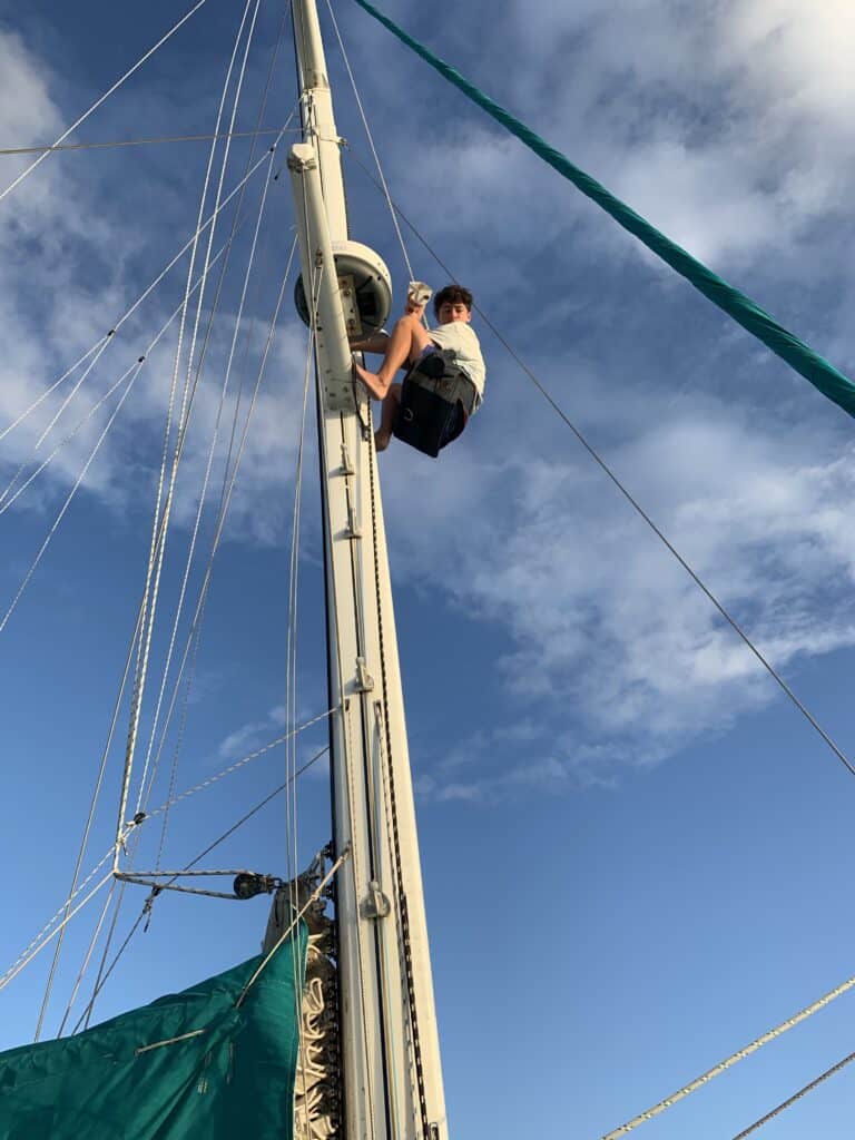 a boy in a bosun's chair climbing up the mast of a sailboat