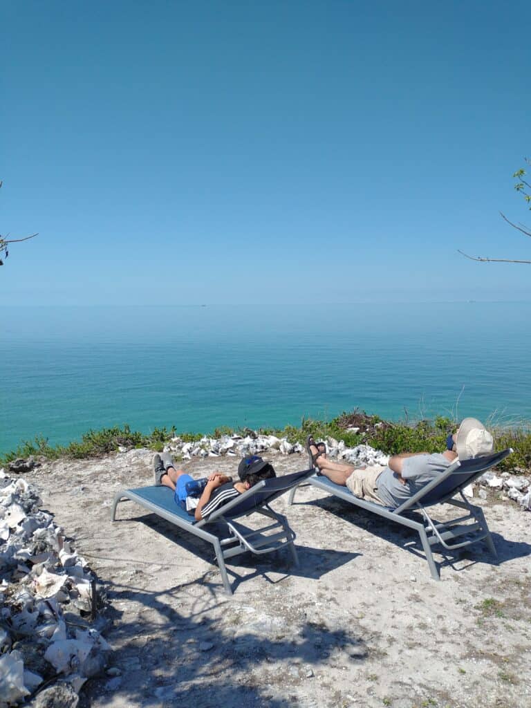 Two people in lounge chairs, looking towards the water, from a hill, in Great Harbour Cay.