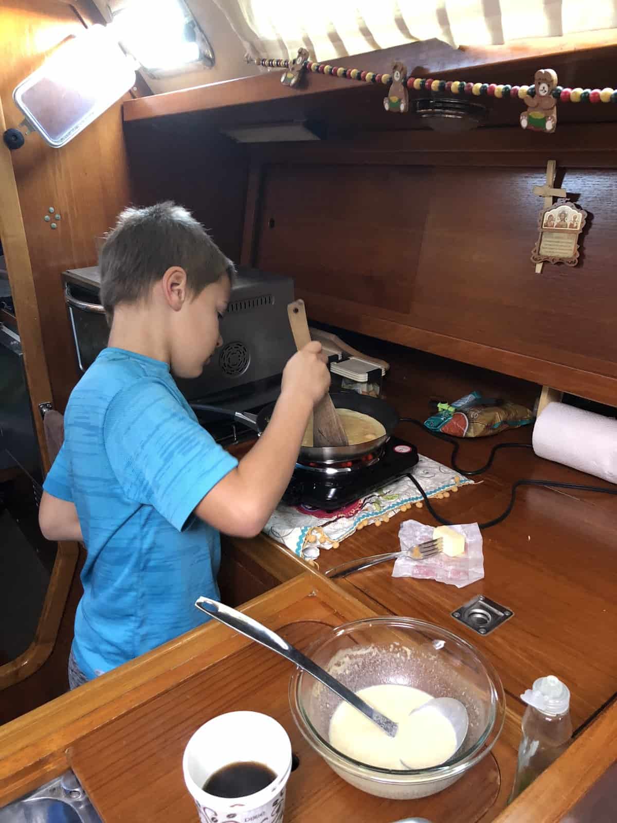 a boy mixing and baking pancakes in the galley of a boat