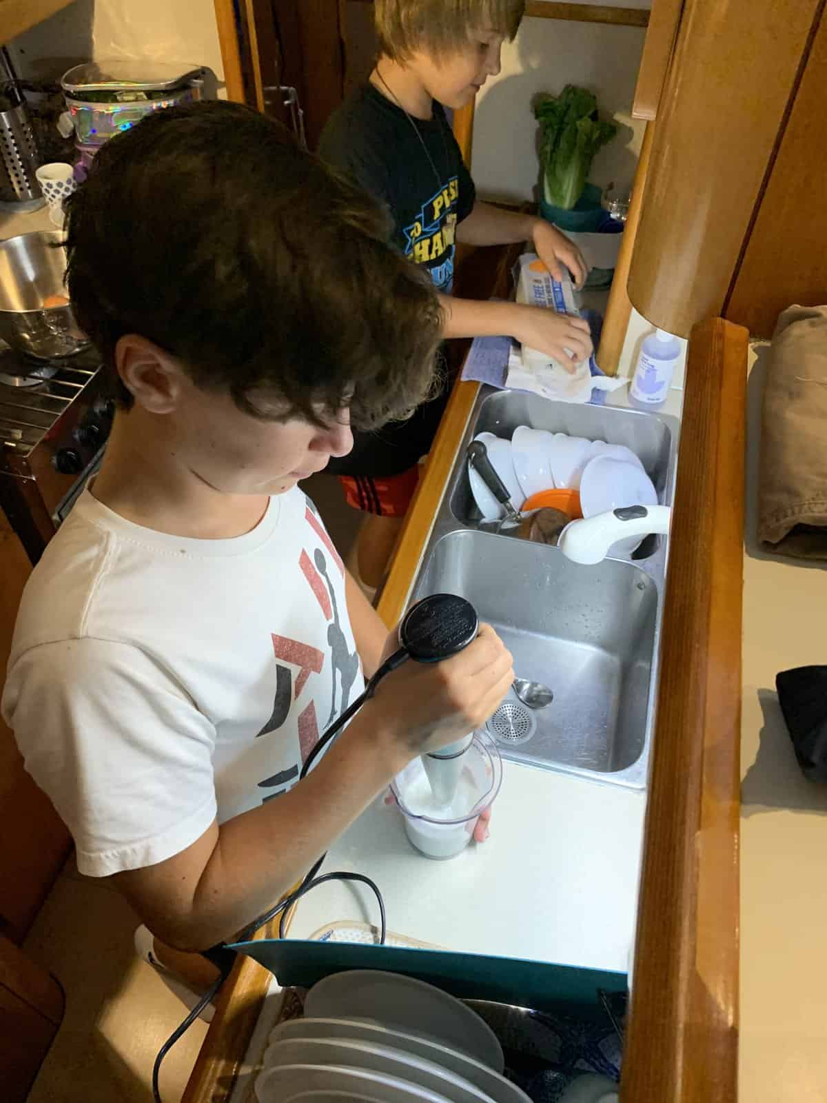 a boy using a hand-held blender to cook aboard a boat