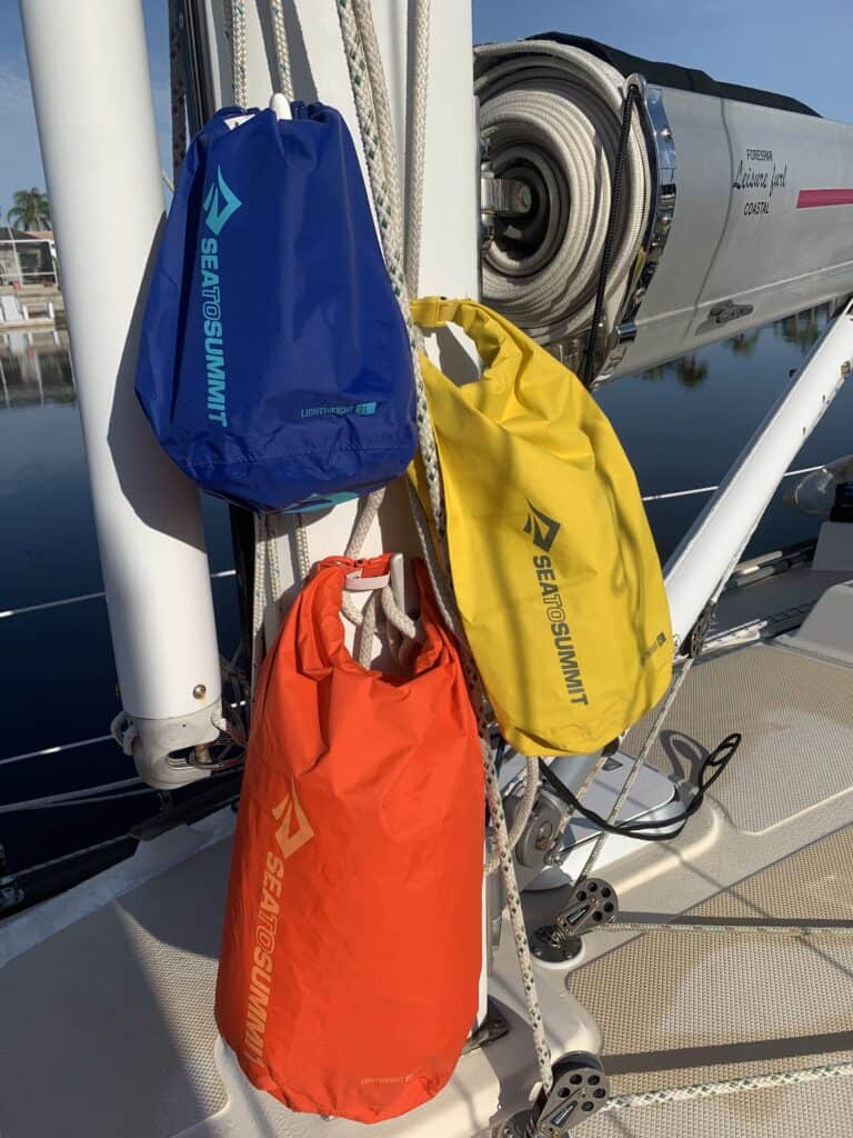 three dry bags of various sizes and colors, hanging on a mast of a sailboat